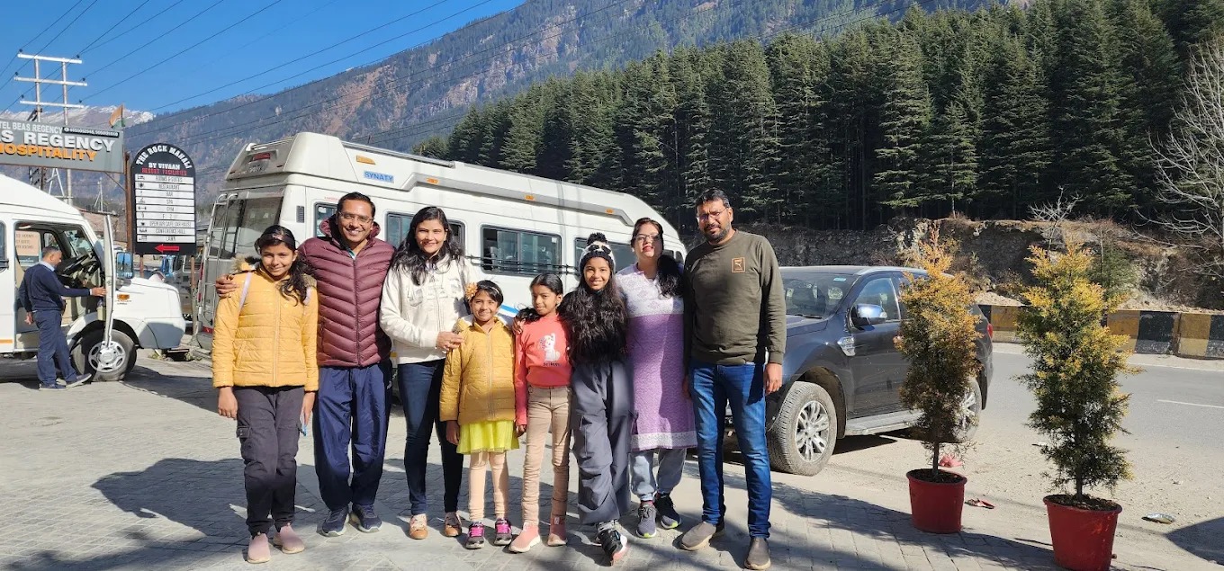 Happy family group posing next to a luxury Tempo Traveller in Delhi